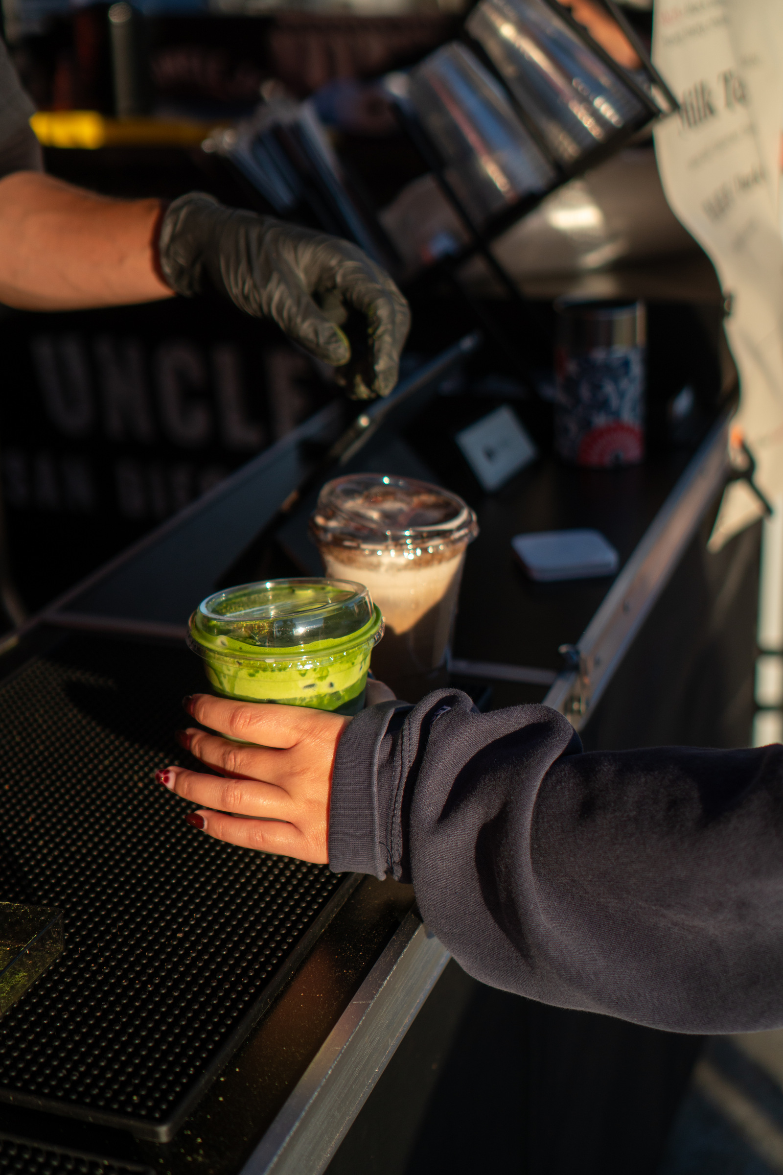 A gloved hand holding an iced Iro Tea drink at the bar