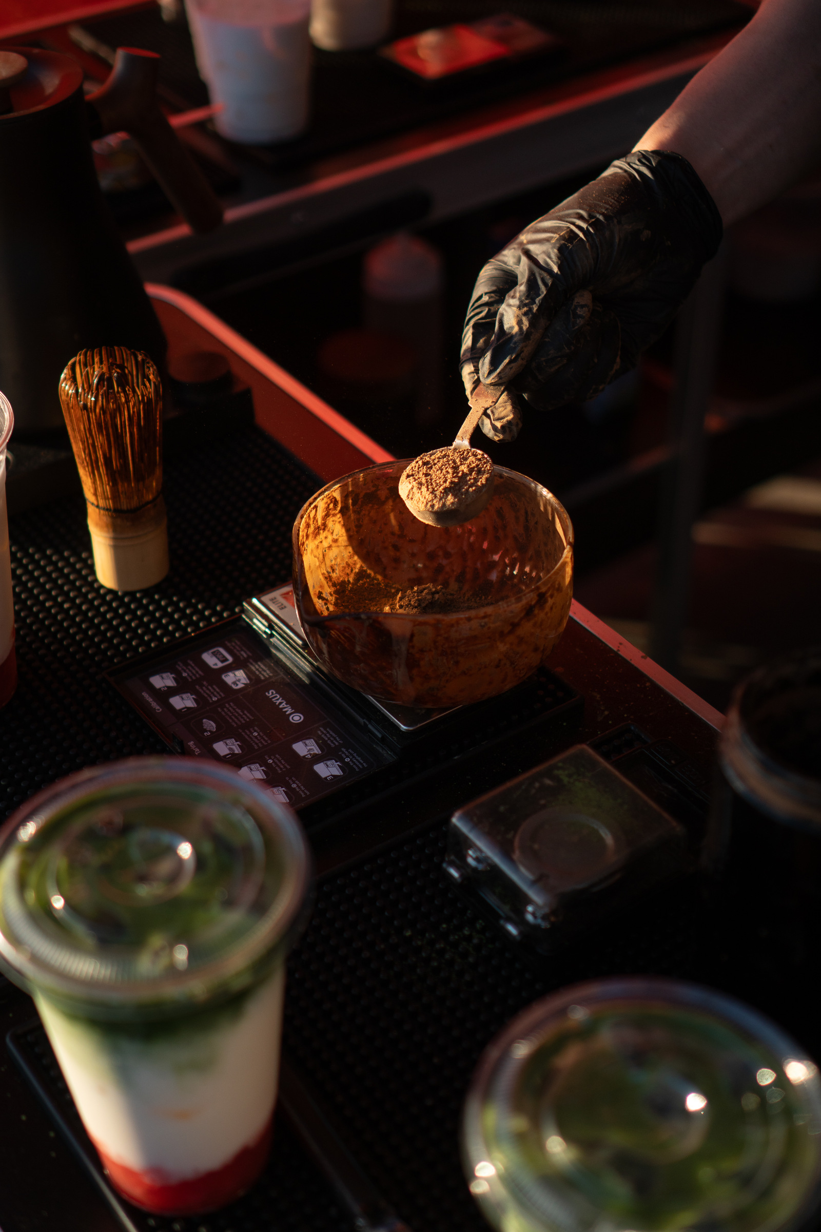 Tea powder weighed on a digital scale beside a bamboo whisk at the R&D bench