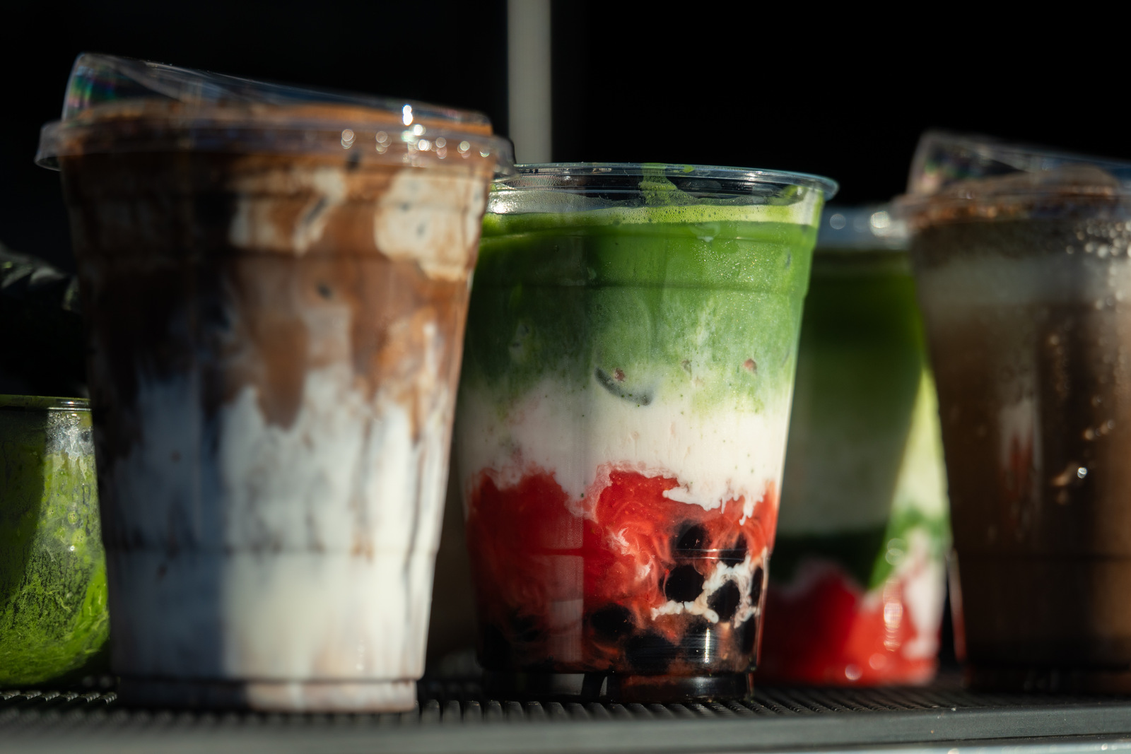 A lineup of layered iced Iro Tea drinks in branded cups, seen in section