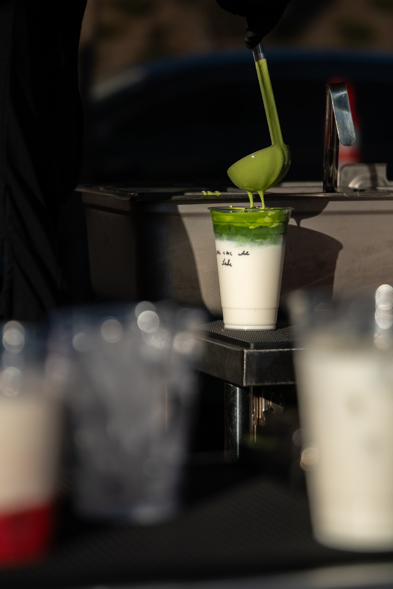 Bright green matcha being ladled over milk into a cup at the market bar