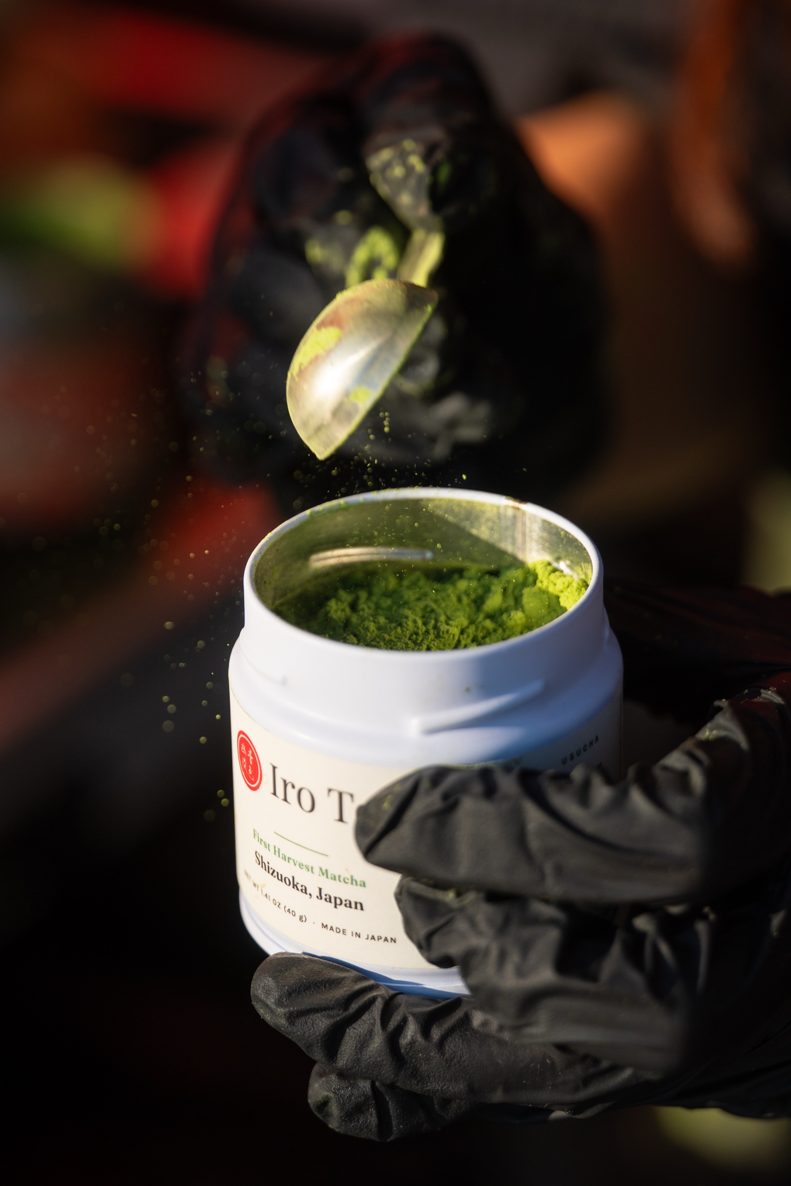 Matcha dust drifting from a scoop into the open M099 tin
