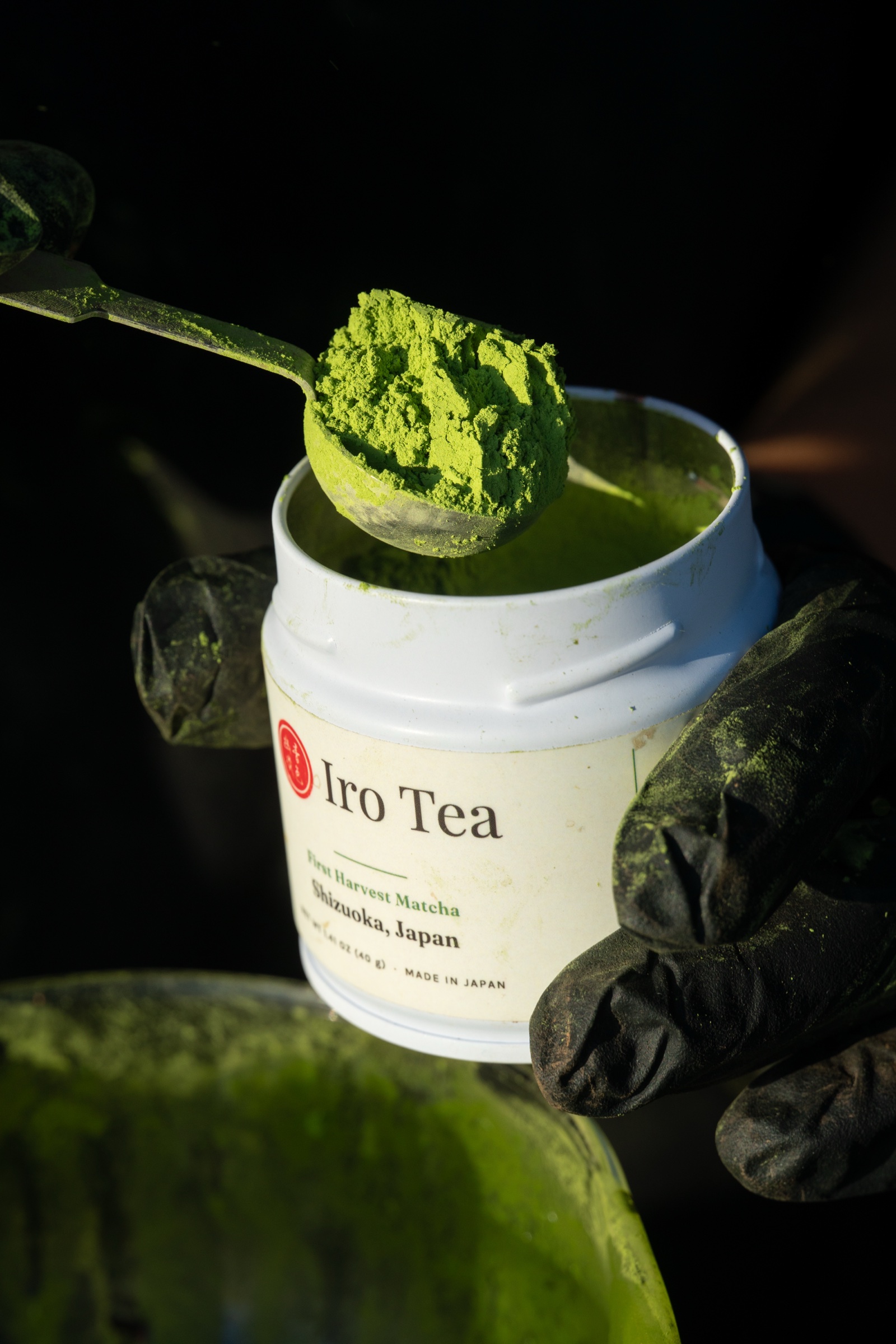 A heaped scoop of vivid green M099 matcha held over the open Iro Tea tin