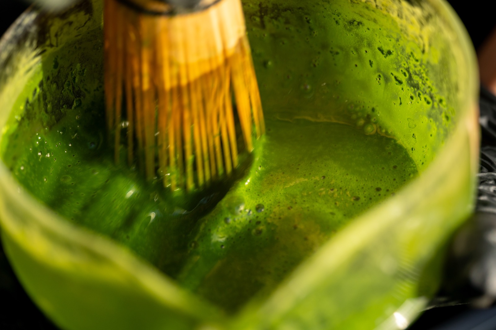 A bamboo chasen whisking vibrant green matcha in a glass bowl