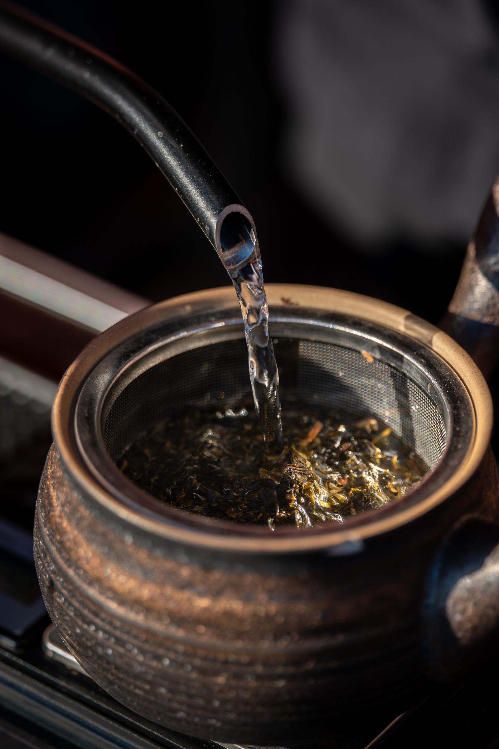 Loose tea leaves steeping through a strainer in a ceramic pot